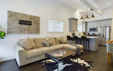 Modern living room with a cozy 4-seater couch, 55-inch TV, foosball table, and Hypebeast decor, including Supreme wall art. A twin roller is available for extra sleeping upon request. This space perfectly blends comfort and trendy vibes for your stay.