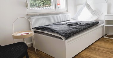 Helle Einzelzimmer mit funktionaler Ausstattung: Bett, Schrank und Sitzgelegenheit – ideal für längere Aufenthalte mit Privatsphäre.