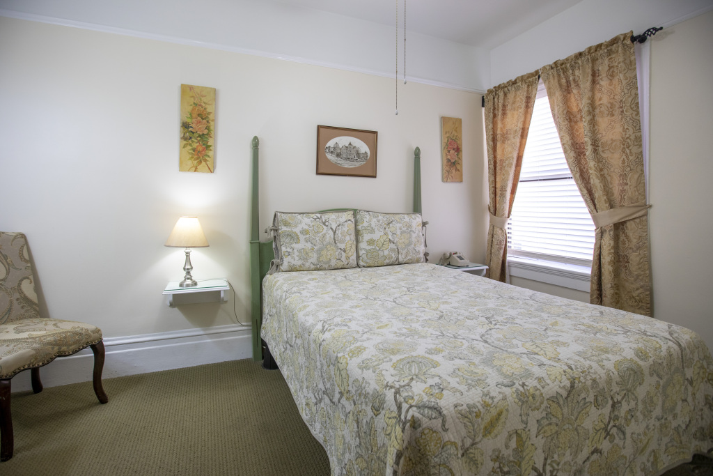 A hotel room with a bed, chair, lamp, and window.
