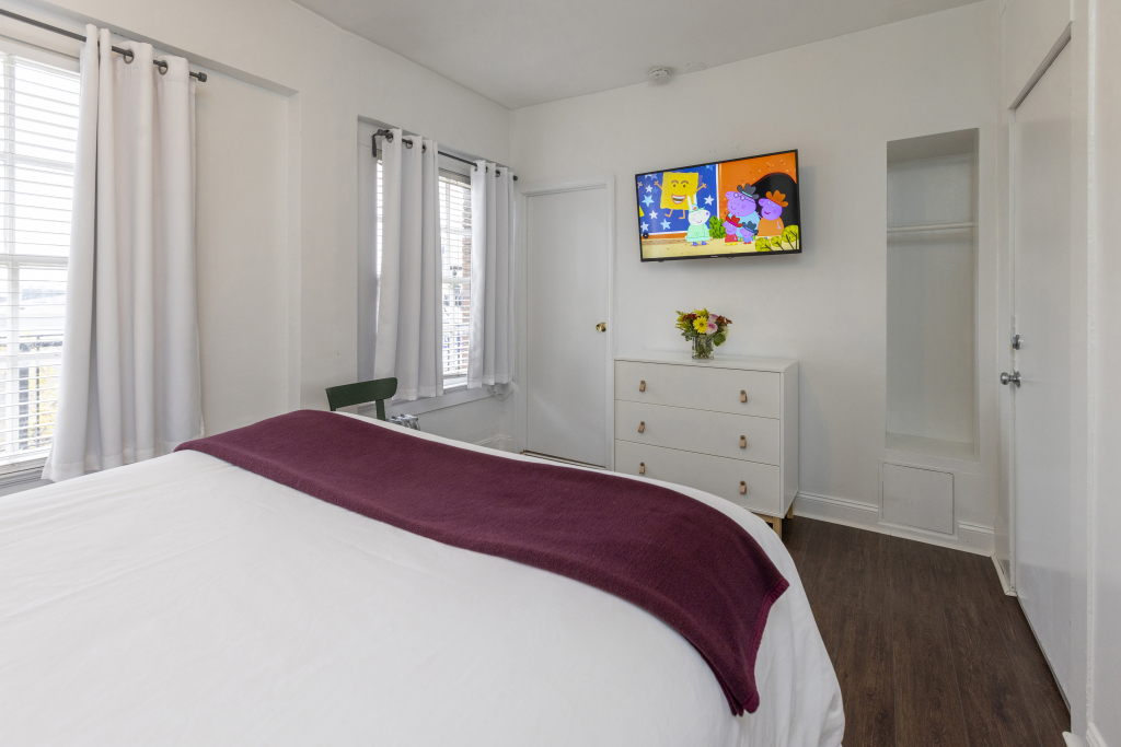 A bedroom with a bed, TV, dresser, and window
