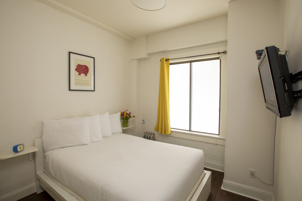 A hotel room with a bed, TV, and window