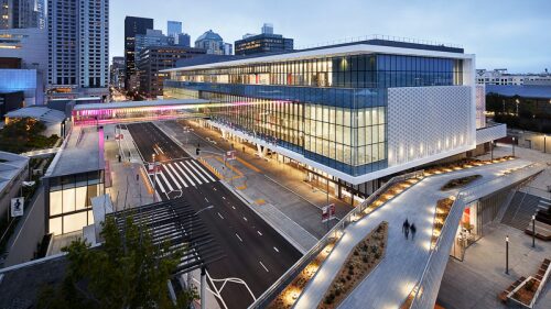 A modern hotel building with a glass facade and a city street view at evening.