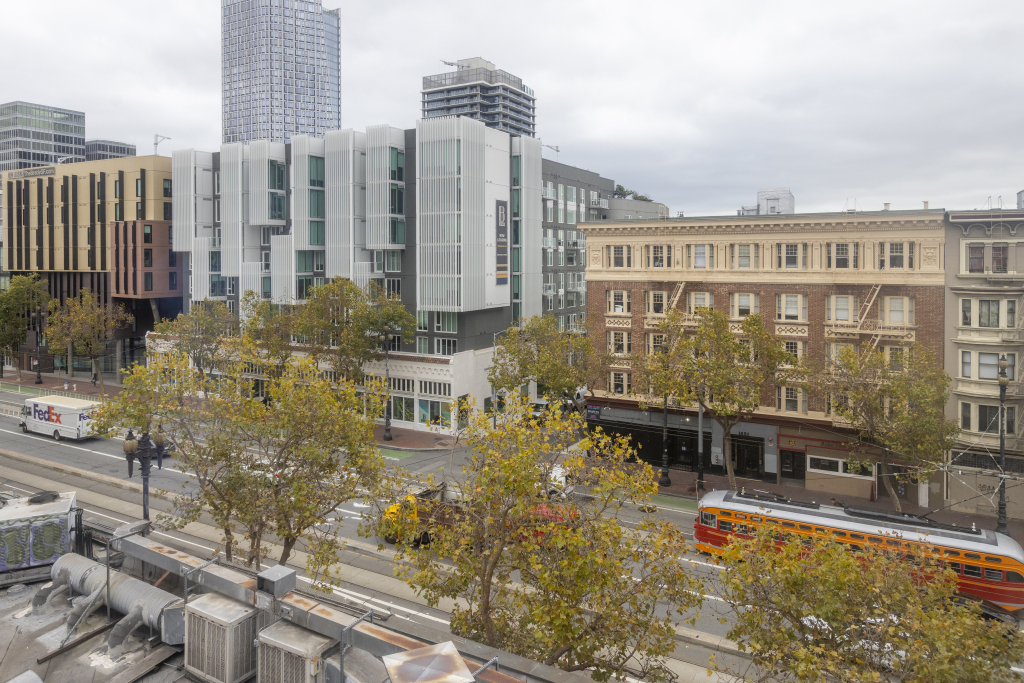 A city street with various buildings, trees, and vehicles.