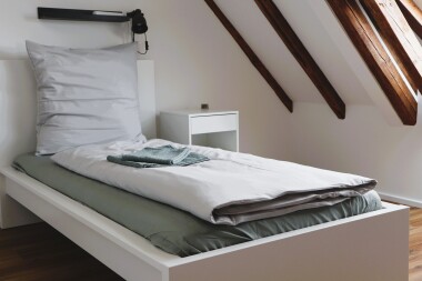 Helle Einzelzimmer mit funktionaler Ausstattung: Bett, Schrank und Sitzgelegenheit – ideal für längere Aufenthalte mit Privatsphäre.