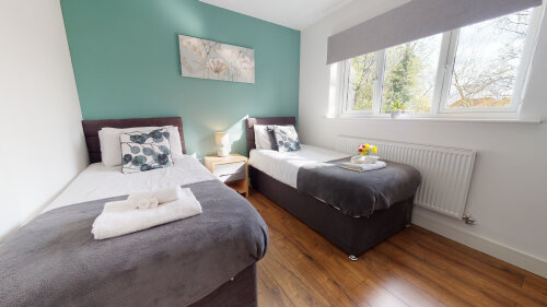 SRK Serviced Accommodation - Bedroom 2 with beautiful pastel colour feature wall. Bedside lamp and wardrobe. Large window giving plenty of natural light.