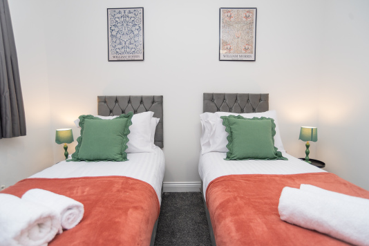 Bright twin bedroom with two single beds, dressed in crisp fresh linens and supplied with soft towels — a clean, colourful and comfortable space for a great night’s rest.