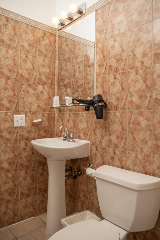 A bathroom with a pedestal sink, toilet, and tiled walls