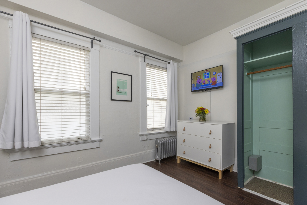 A white bed and dresser in a room with windows and a closet.