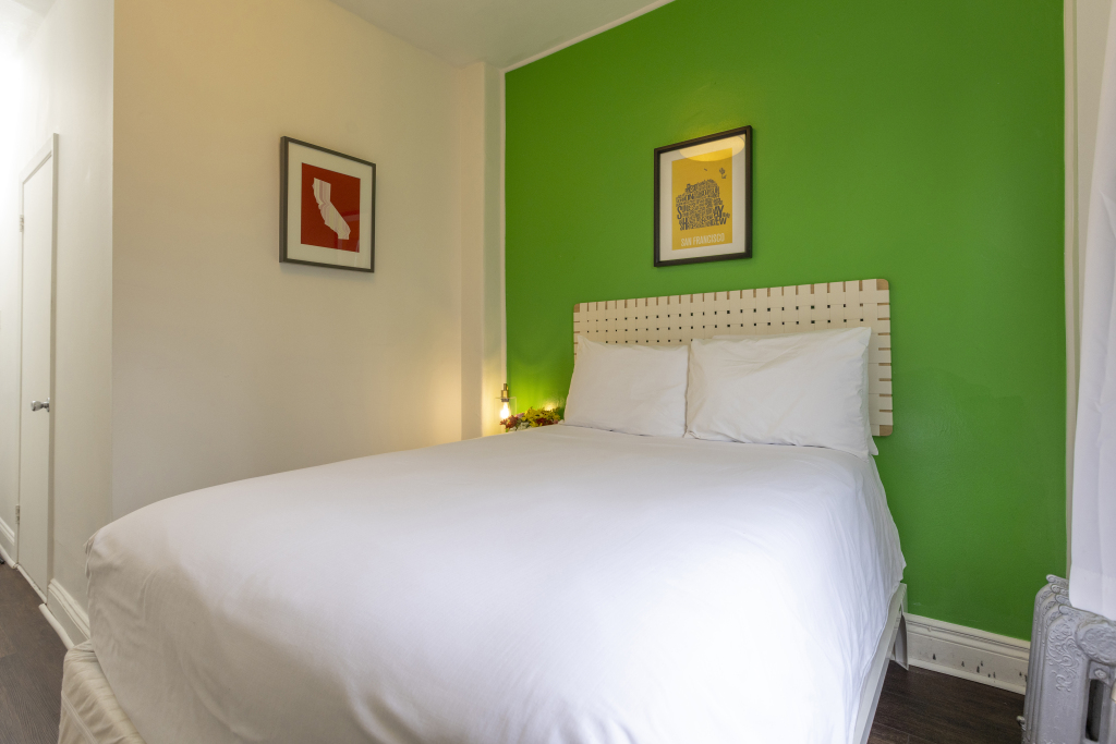 A hotel room with a large bed, white bedding, and green accent wall.