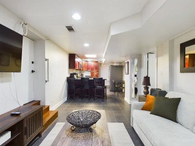 This cozy living room features a plush sofa, a sleek wall-mounted TV, and modern decor. Adjacent to the stylish kitchen with bar seating, it’s the perfect space to relax or entertain with friends. The open layout ensures a warm, inviting atmosphere!