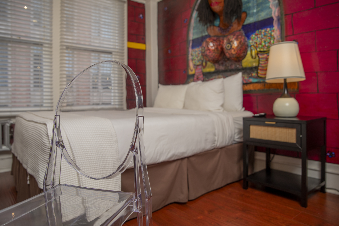 A hotel room with a bed, chair, lamp, and artwork.