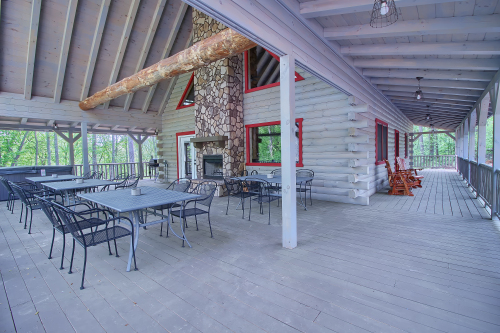 Left side Porch, with Outdoor Dining Tables and Wood-Burning Outdoor Fireplace and Hot Tub, front porch to right,  Rustic Cedar Inn 