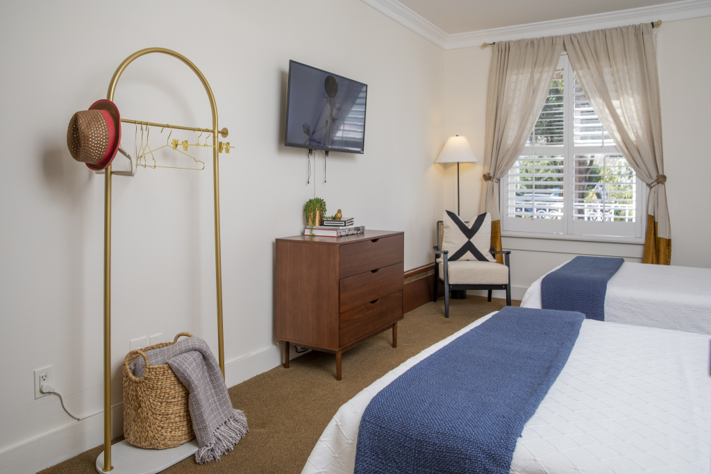 A hotel room with two beds, a dresser, TV, chair, and window.