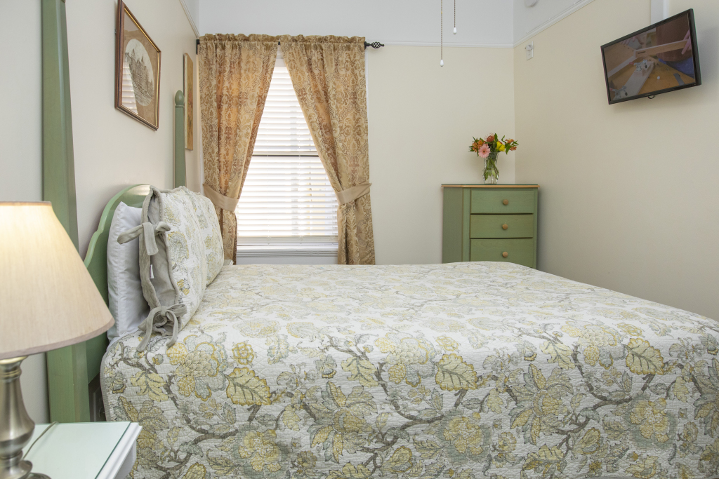 A wide view of a bedroom with a bed, dresser, TV, and lamp.