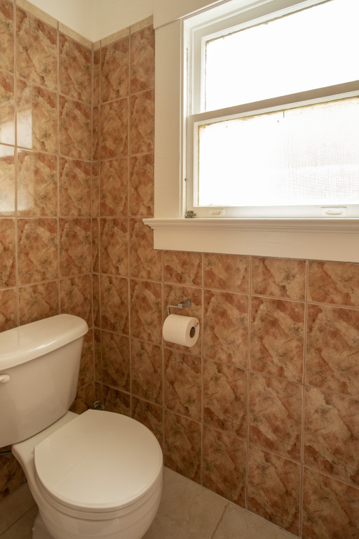 A bathroom with a toilet, tiled walls, and a window.