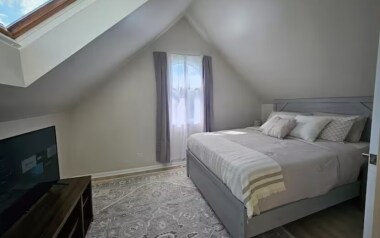 This cozy bedroom features a comfortable queen-size bed and a 40-inch TV for your entertainment. The room’s sloped ceilings and soft natural light create a peaceful and inviting retreat, perfect for relaxing after a day of exploring the city.