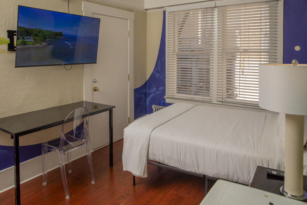 A hotel room with a bed, desk, TV, and lamp.
