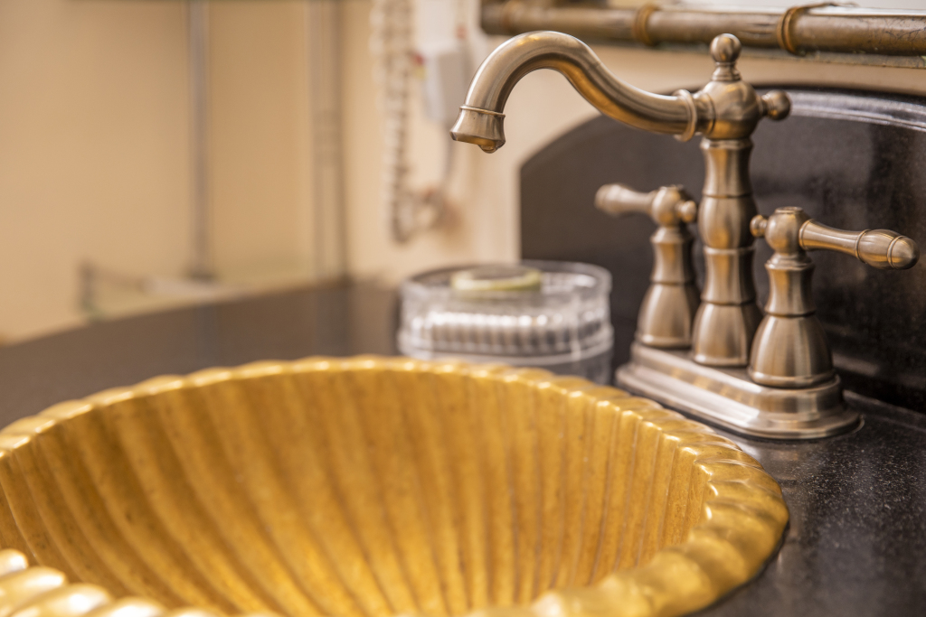A close-up of a gold sink with a brass faucet on a black countertop.