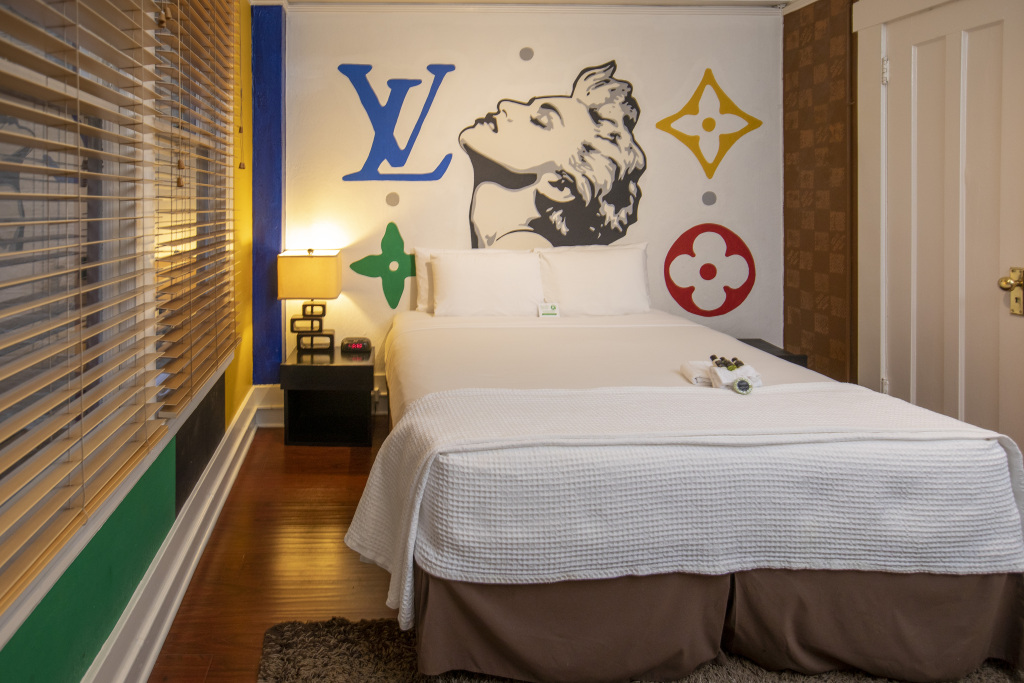 A hotel room with a large bed, colorful wall art, and a window with blinds.