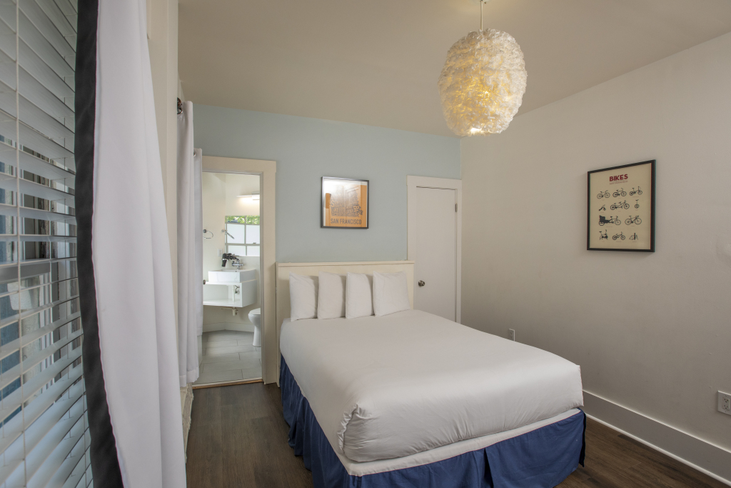 A hotel room with a bed, chandelier, artwork, and bathroom