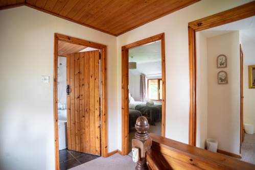 Upstairs hallway with pine ceiling and trim, showing open doors to a bathroom with bath visible and a twin bedroom.