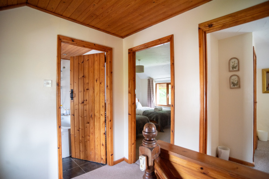 Upstairs hallway with pine ceiling and trim, showing open doors to a bathroom with bath visible and a twin bedroom.