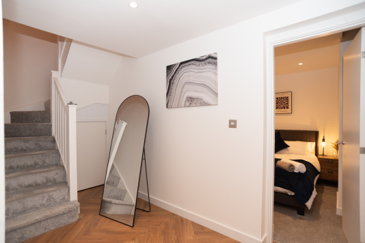 A bright, open hallway connecting the downstairs bedrooms to the main floor with kitchen, dining and living areas plus the master bathroom — a spacious two-level apartment with three bedrooms sleeping up to 8 guests.