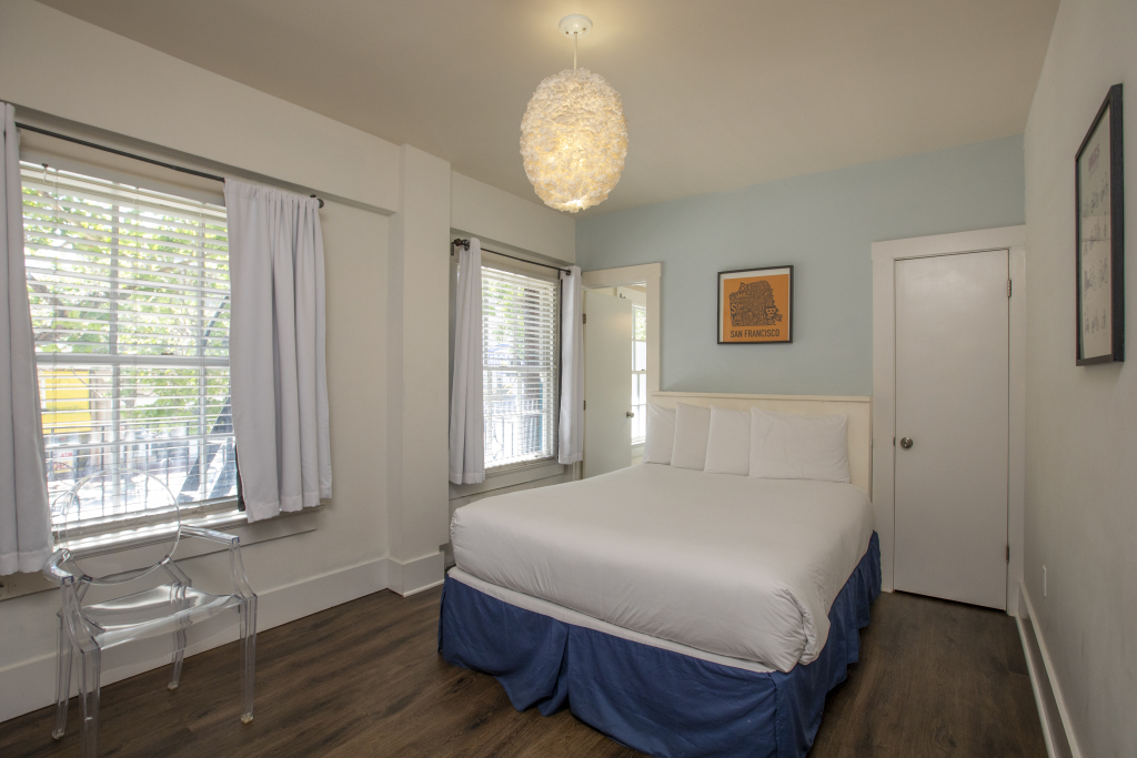 A hotel room with a bed, window, door, chair, and light fixture.