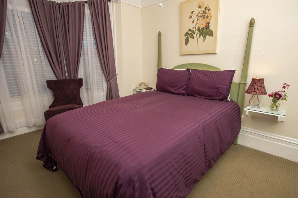 A wide view of a bedroom with a purple bed, chair, and curtains.