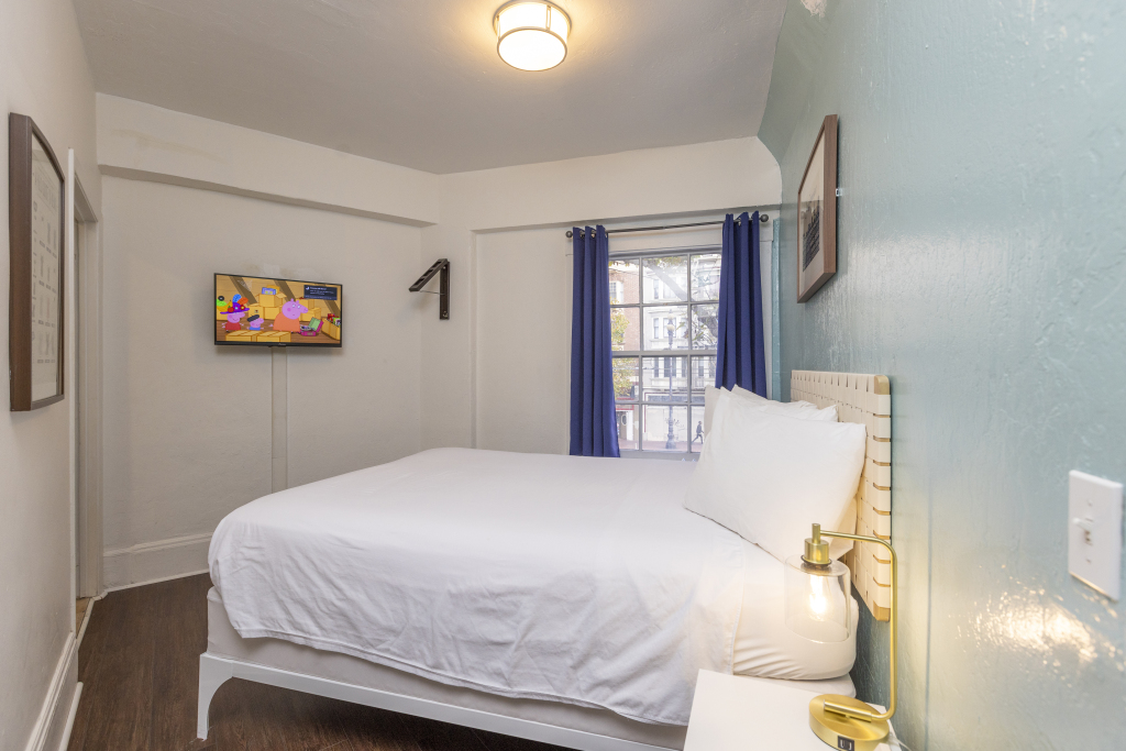 A hotel room with a bed, TV, and window