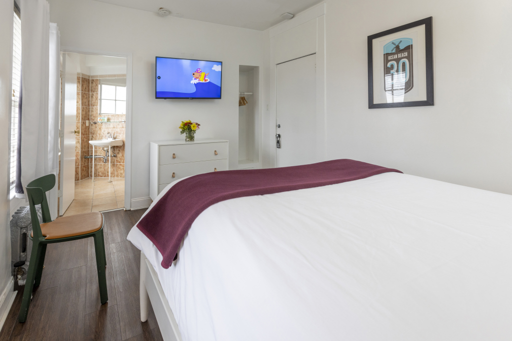 A hotel room with a bed, TV, dresser, chair, and door.