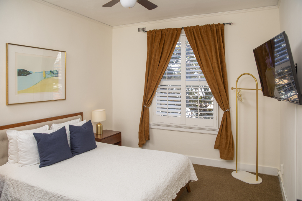 A hotel room with a bed, window, TV, and artwork.