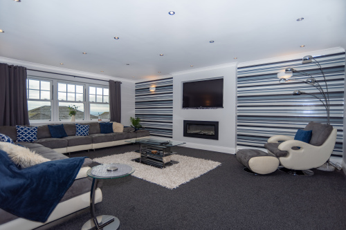 Expansive living room with generous seating for groups, a 4K smart TV, and a feature fireplace for cosy winter evenings, all framed by beautiful sea views.