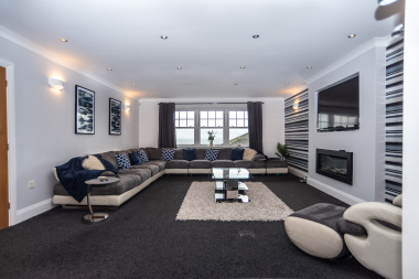 Expansive living room with generous seating for groups, a 4K smart TV, and a feature fireplace for cosy winter evenings, all framed by beautiful sea views.