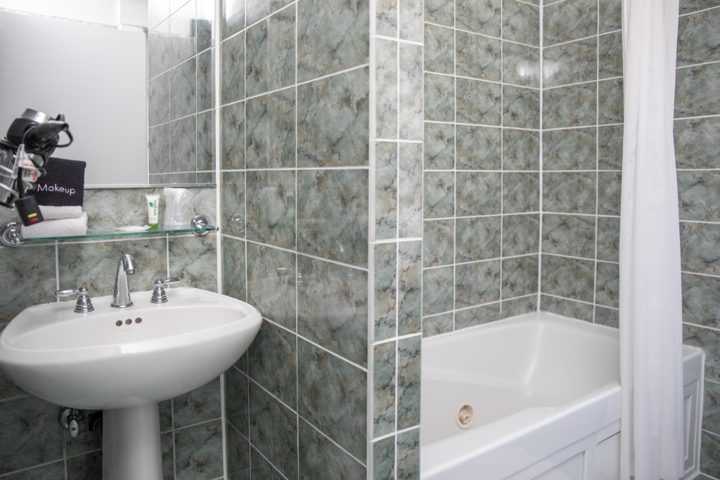 A bathroom with a sink, bathtub, and greenish marble tiles