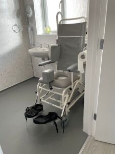 The en-suite wet-room has a step-free shower, fixed grab-rails for WC, shower, and washbasin, drop-down grab-rail alongside WC, wheeled commode shower chair, tilting shower chair, and lever-style taps.