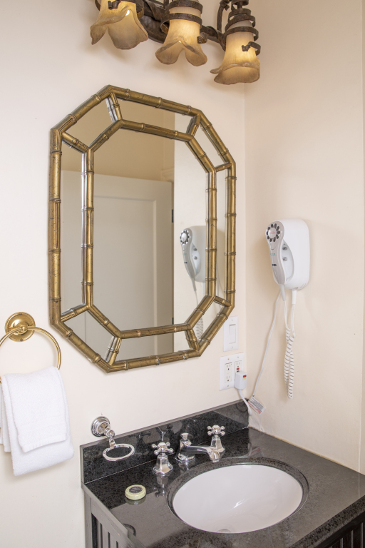 A bathroom with a gold mirror, black countertop, and white sink.