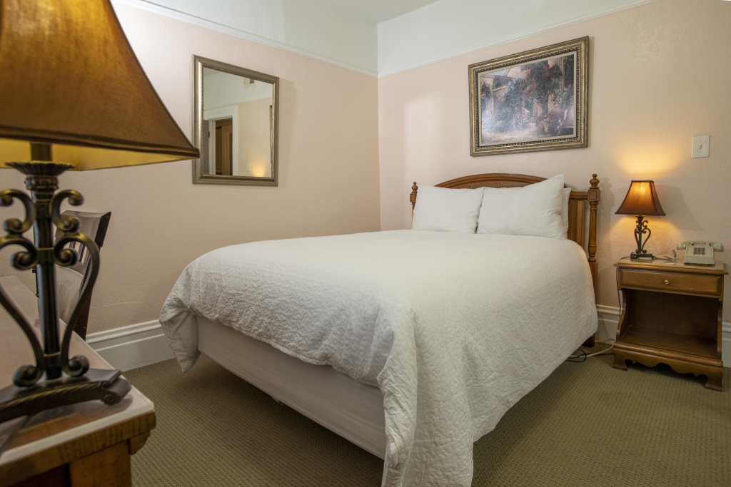 A hotel room with a bed, nightstand, lamp, mirror, and painting.
