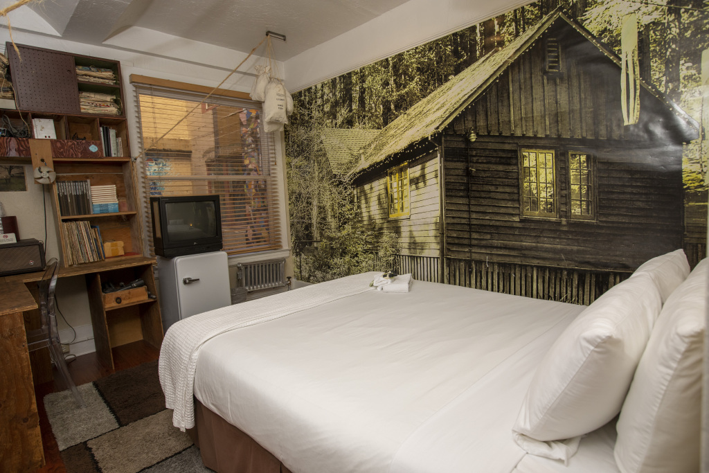 A hotel room with a large bed, desk, bookshelf, and TV