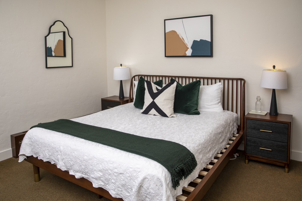 A neatly made bed with pillows and a throw blanket in a room with artwork and a mirror on the wall.