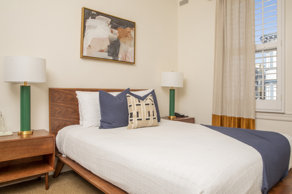 A neatly made bed with pillows and a painting on the wall in a hotel room.