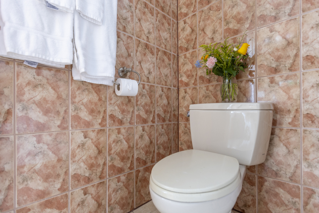 A bathroom toilet with tiled walls, a vase of flowers, and a stack of white towels.