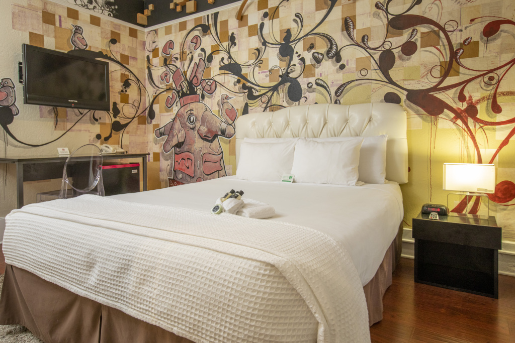 A hotel room with a large bed, tufted headboard, and colorful wall art.