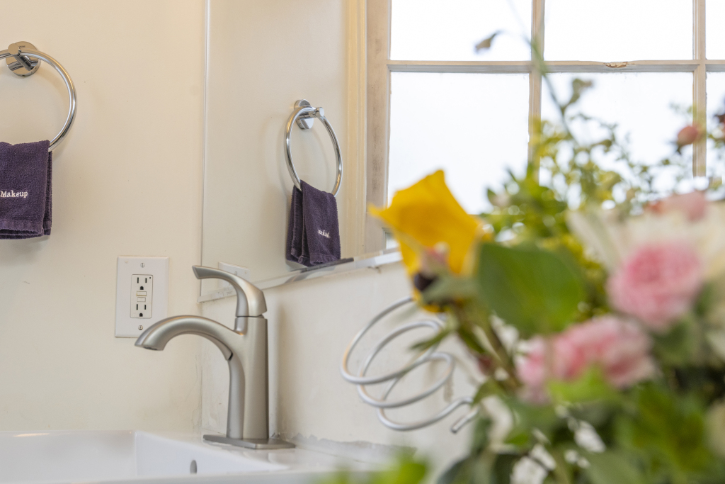 A bathroom sink with a silver faucet, purple towels, and flowers in the foreground.