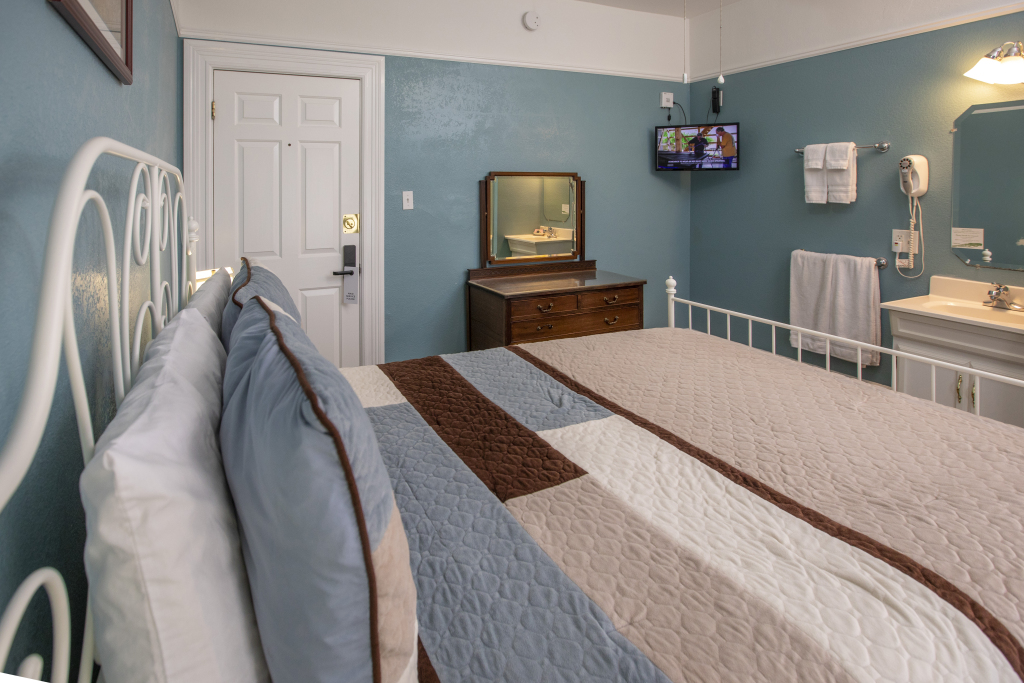 A hotel room with a large bed, TV, vanity and door