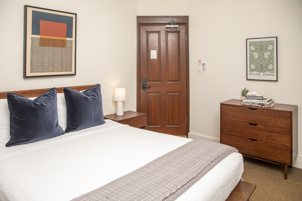 A neatly arranged hotel room with a bed, dresser, nightstand, and artwork.