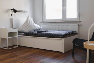 Helle Einzelzimmer mit funktionaler Ausstattung: Bett, Schrank und Sitzgelegenheit – ideal für längere Aufenthalte mit Privatsphäre.