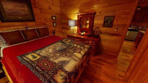 The master bedroom on the main floor features ultimate comfort in bedding, lighting and decor, a HD Smart TV, rustic log furniture and ceiling fan, hand-peeled logs adorning the ceiling, and more!