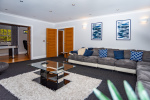 Spacious living room with soft night lighting and large comfortable sofas, flowing into a beautifully styled games room featuring a pool table.