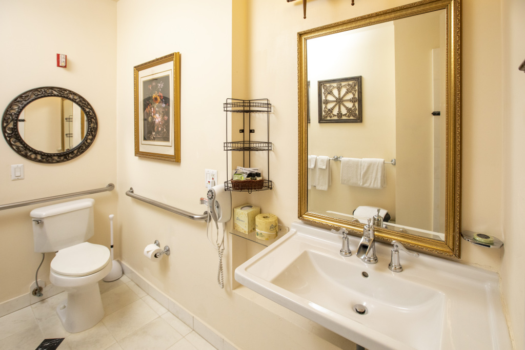 A standard bathroom with a toilet, sink, and mirror, featuring grab bars for accessibility.